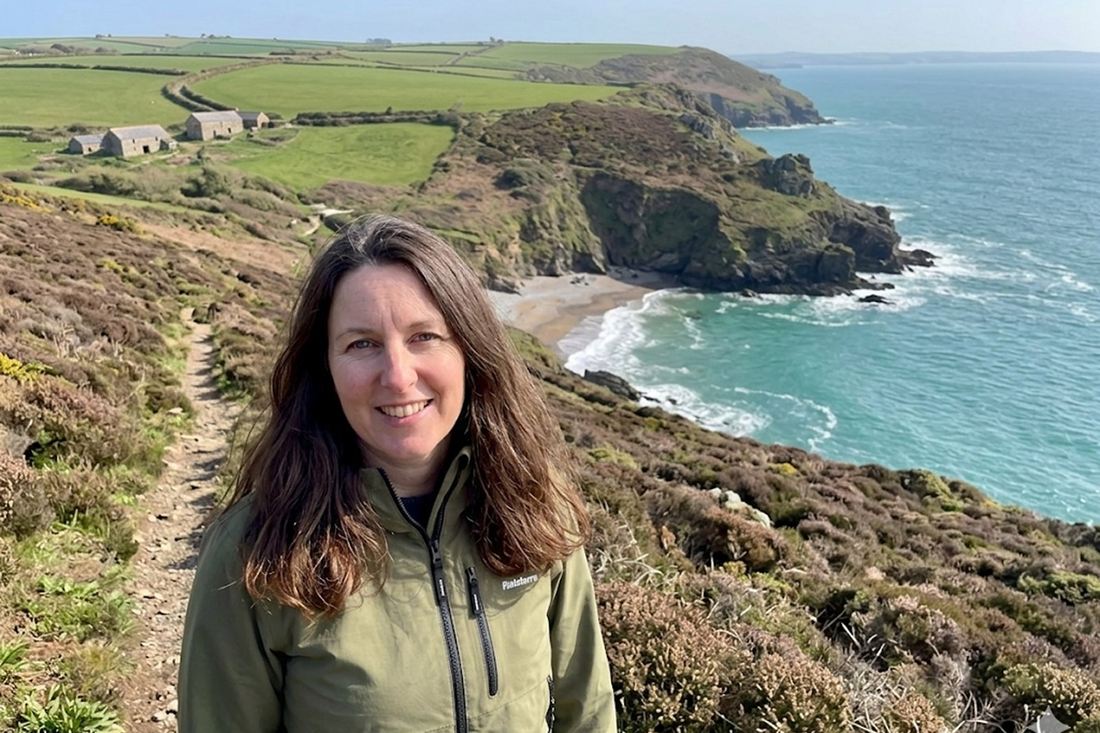 Anna on a coast path in spring, the sea and cliffs behind her.