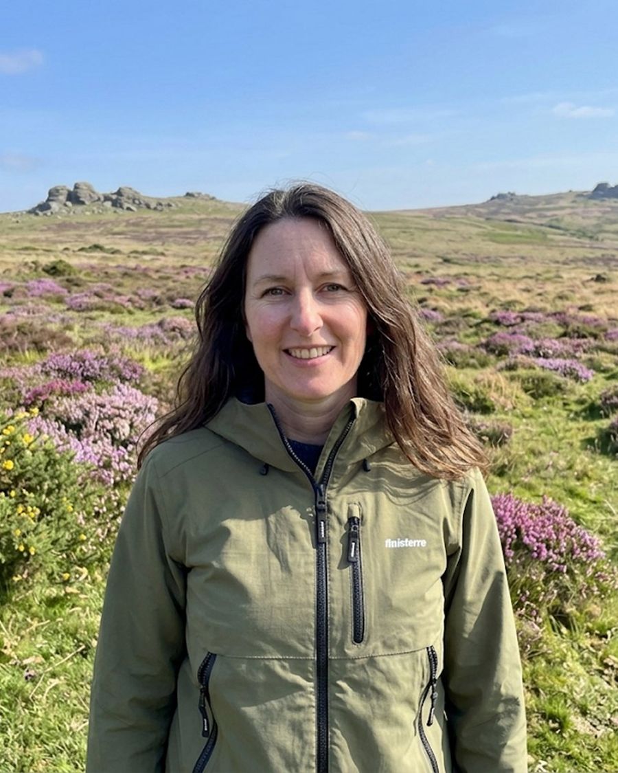 Anna standing on Dartmoor in late summer, heather in flower around her and a tor on the skyline behind.