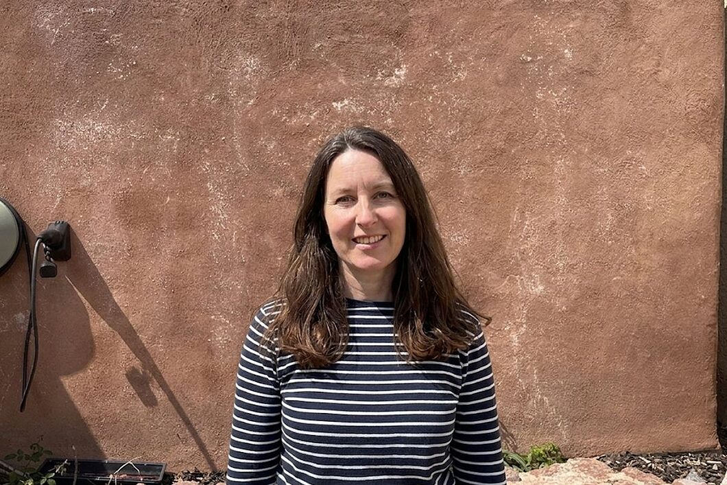 Anna at home, standing against the cob wall of the house.